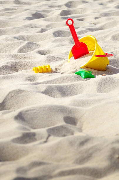 Brightly colored plastic sand toys, including buckets, shovels, and molds, scattered on a sunny beach. The sandy surface showcases playful textures and a warm outdoor summer vibe, evoking a sense of joyful beach activity.