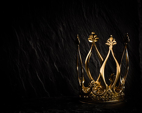 Royal gold crown on dark stone surface. Concept of wealth, success and kingdom.