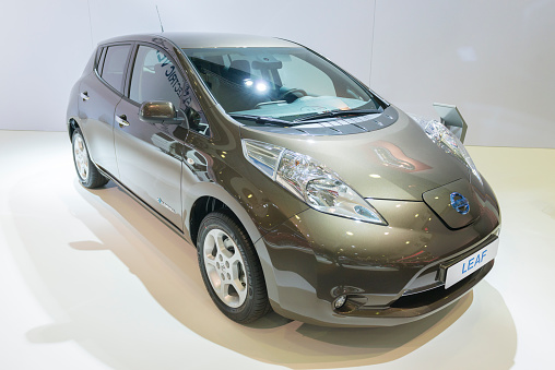 Brussels, Belgium - Januari 12, 2016: Green Nissan Leaf full electric car front view. Leaf stand for leading environmentally-friendly affordable family car and it is an an all-electric car, that  produces no tailpipe pollution or greenhouse gas emissions. The car is on display during the 2016 Brussels Motor Show. The car is displayed on a motor show stand, with lights reflecting off of the body.