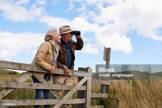 Coppia Senior Con Binocolo Cammina In Campagna - Fotografie stock e altre immagini di Osservare gli uccelli - Osservare gli uccelli, Terza età, Binocolo