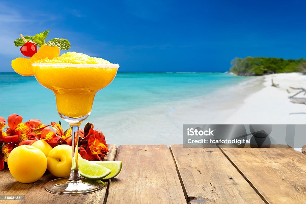 Peach daiquiri on wood table against tropical beach background Peach daiquiri on wood table against tropical beach background. The glass is placed at the left of the frame leaving a useful copy space at the center-right Beach Stock Photo