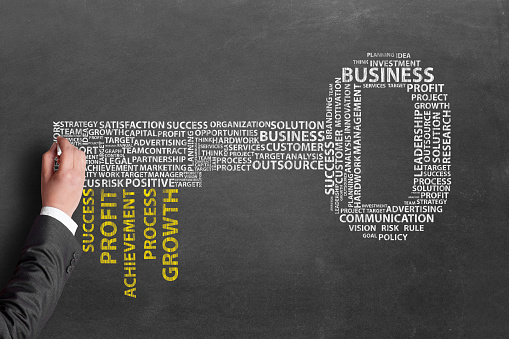 Close-up of businessman's hand pointing at business word cloud concept on chalkboard. Word cloud on chalkboard which forming the shape of key to success.