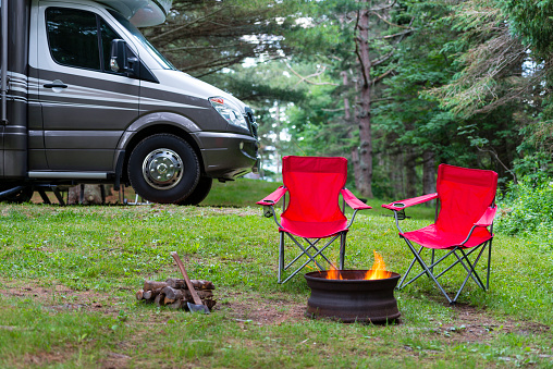 Two red folding chairs near campfire. Motor Home in background.