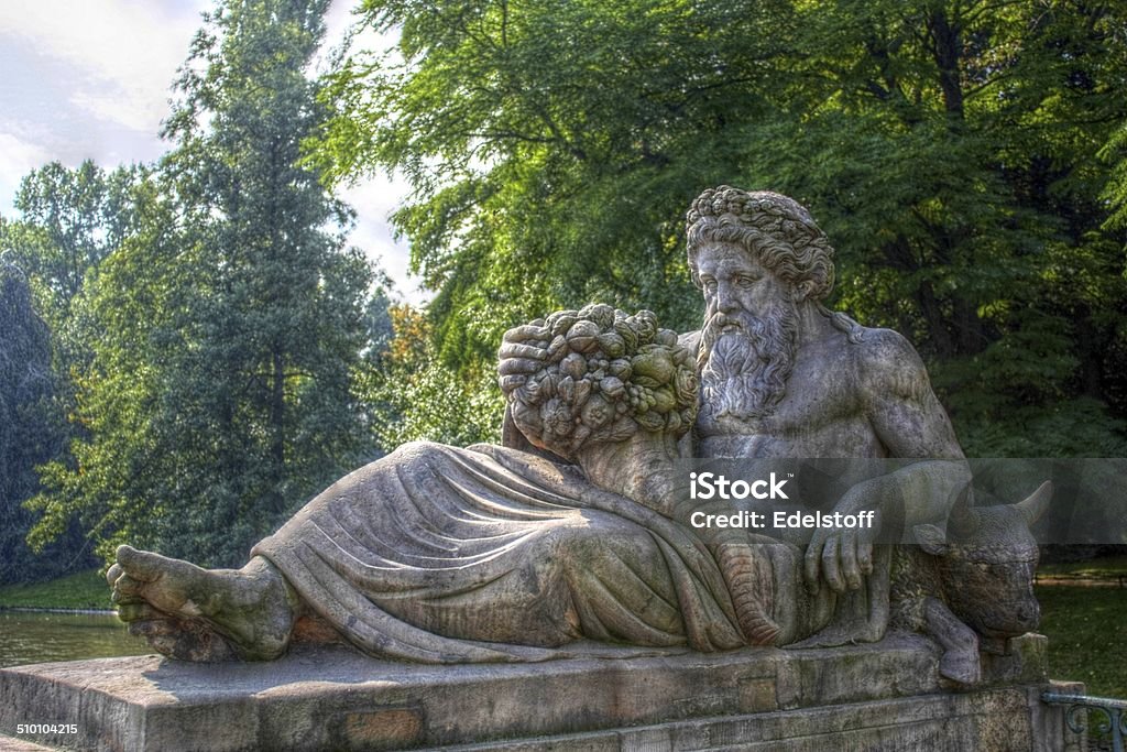Dionysus statue in Lazienki Park, Poland Statue of Dionysus carved from stone situated in front of a pond in Lazienki Park, Warsaw. This HDR picture shows the figurine of the Greek god resting with a cornucopia in his hand and a calf beside him. Dionysus, like his Roman equivalent Bacchus symbolizes grape harvest, winemaking and wine, ritual madness and religious ecstasy in Greco-Roman mythology. Wine Stock Photo
