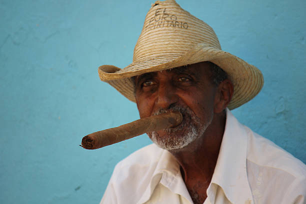 Old man smoking a typical cuban cigar Trinidad, Сuba - August 18, 2012: Trinidad, Cuba, August 19, 2012. An old man with panama hat smoking a typical cuban cigar, a very long one. cuban man smoking big cigar stock pictures, royalty-free photos & images