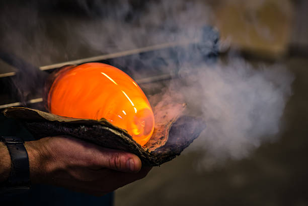 Glassblowing Glass blower shaping the glass with a piece of wet newspaper. Intentional motion blur of glass in picture. hand blown glass stock pictures, royalty-free photos & images