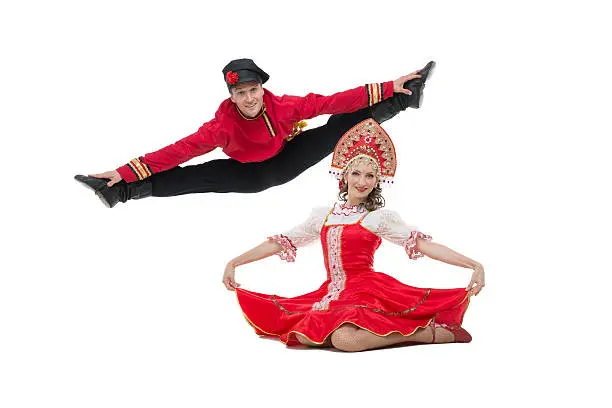 Couple of dancers in russian traditional costumes, girl in red sarafan and kokoshnik, boy in black trousers and red shirt . Man makes a jump. Studio shot isolated on white.