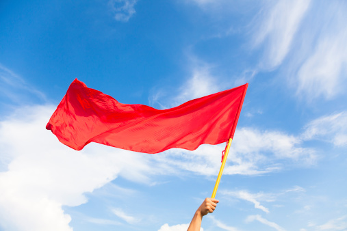 Hand waving a red flag with blue sky background in outdoors