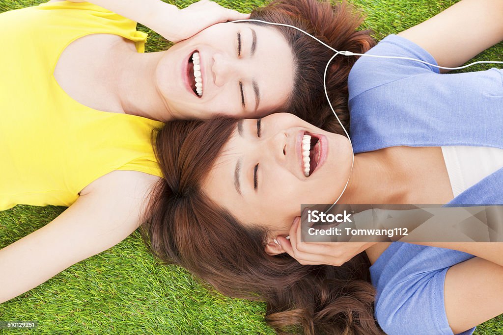 two pretty young woman lying on grassland and listening music two pretty young woman lying on grassland and listening music. Adult Stock Photo