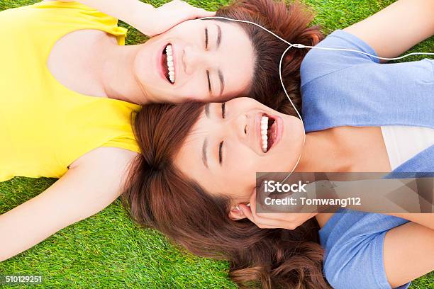 Two Pretty Young Woman Lying On Grassland And Listening Music Stock Photo - Download Image Now
