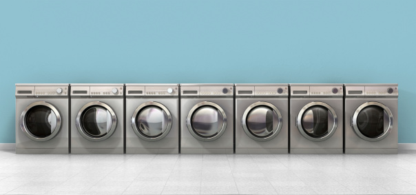 A front view of a row of empty regular brushed metal washing machines in an empty room with a shiny tiled floor and a baby blue wall