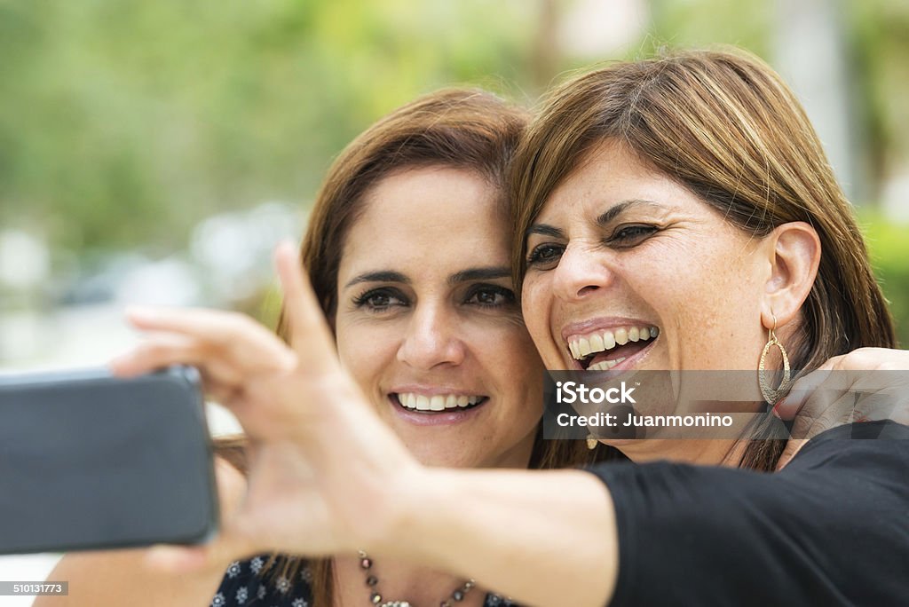 Selfie Smiling mature hispanic women posing together, one is holding her smart phone taking a selfie Family Stock Photo