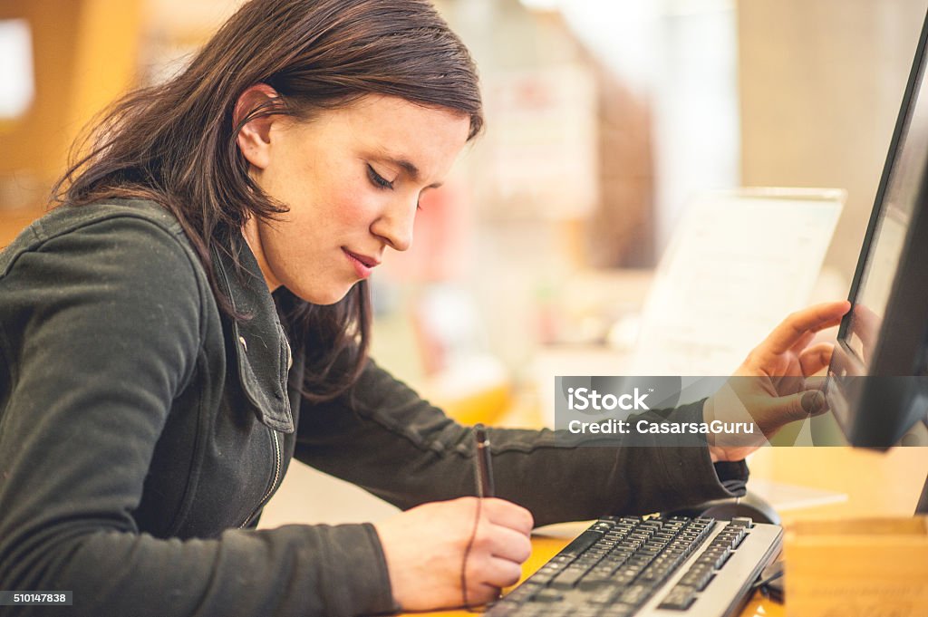 Young Woman Using Computer in Library Young woman using computer in library, writing down, real people 20-24 Years Stock Photo
