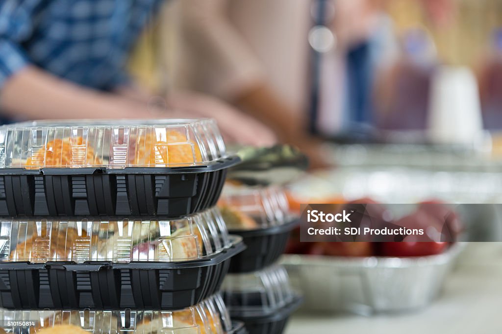 Close up of prepacked food and fruit in soup kitchen Stacks of prepacked food and a serving tray filled with fresh apples on a table at community soup kitchen. Focus is on the stack of prepackaged food. Volunteer is workingin the background. Meal Stock Photo