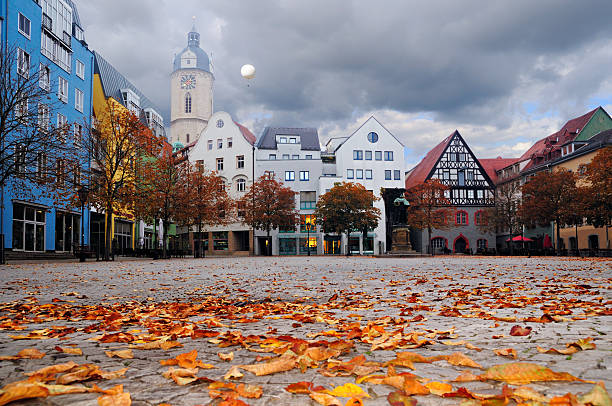Historical buildings facing the market square, still empty in the foggy morning. There is a flying balloon catching a glimps of sun high above. City of Jena, Thuringia, Germany