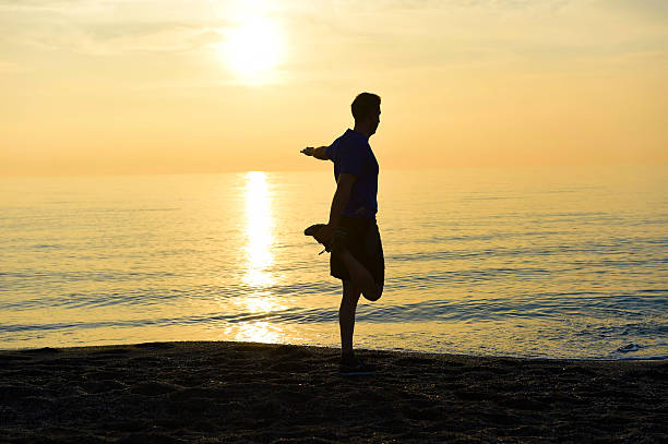 istock silhouette  young sport man stretching leg on beach at sunset 510163434