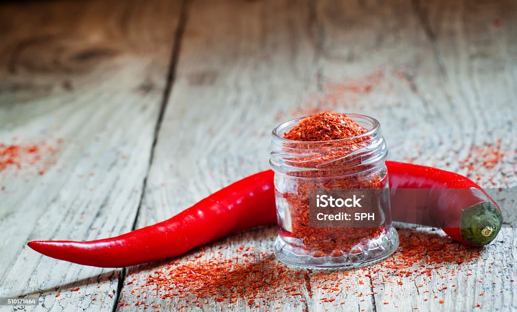 Ground hot red pepper in a glass jar Ground hot red pepper in a glass jar and fresh chili peppers on old wooden background, selective focus Cayenne Pepper Stock Photo