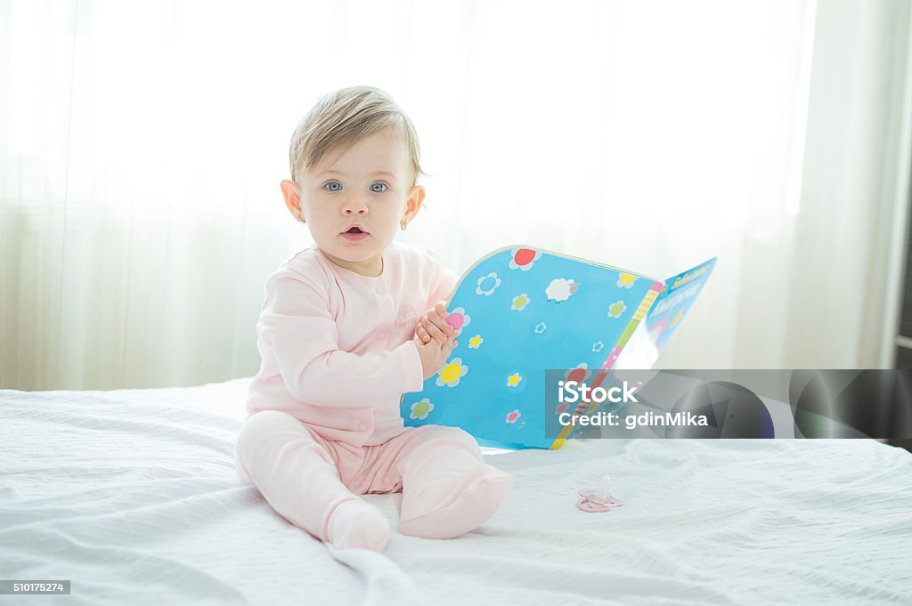 Litle innocent baby reading book on bed Baby - Human Age Stock Photo