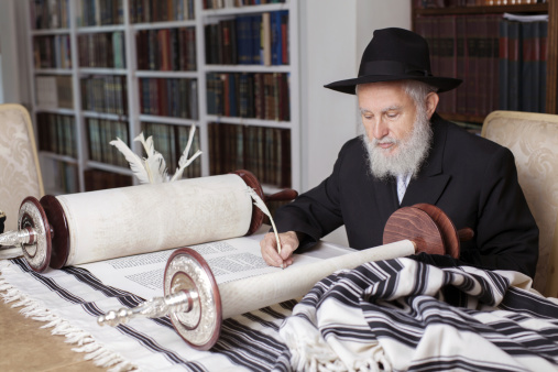 Scribe finishing writing in a Torah scroll. Selective focus on hand and scroll.