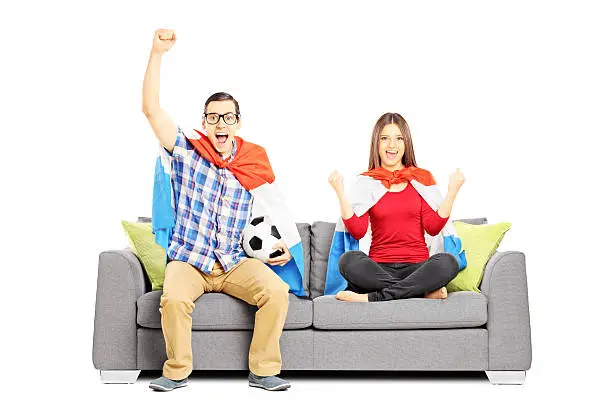 Photo of Young football supporters sitting on a modern sofa