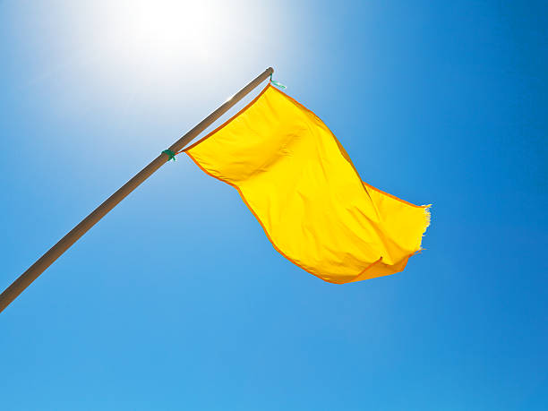 istock warning yellow flag under sun with blue sky 510198789