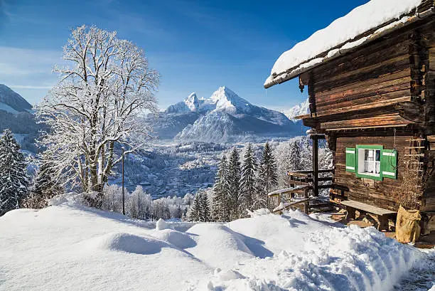 Beautiful winter wonderland mountain scenery in the Alps with traditional mountain chalet on a sunny day.