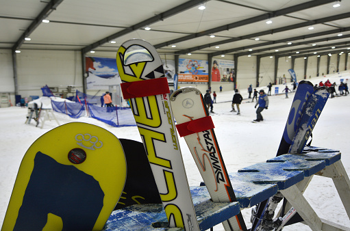 Auckland, New Zealand - July 30, 2015: Snowboarders snowboard down a slope and a rack of skis and snowboards in Snowplanet. It's New Zealand's first indoor snow facility features 50cm of real snow of a terrain park for freestyle skiers, snowboarders and learners sloop