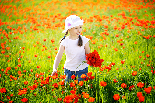Blonde woman wearing a straw bonnet hat looks out to the field of poppy wildflowers during the superbloom