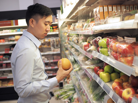 Young Asian man selecting a fruit from supermarket