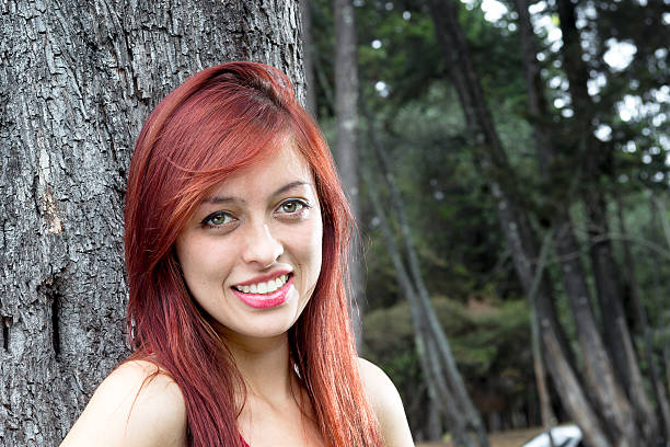 Portrait of young colombian woman from Bogota, standing beside a tree on a city park and looking to the camera.