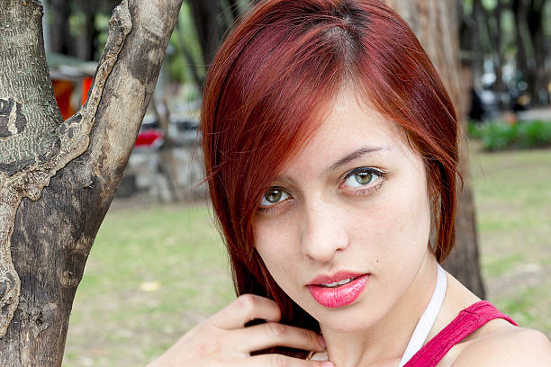 Portrait of young colombian woman from Bogota, standing beside a tree on a city park and looking to the camera.