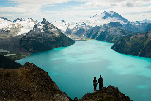 Couple embracing at a stunning vantage point overlooking a glacial lake in British Columbia, Canada's Coast Mountain Range.