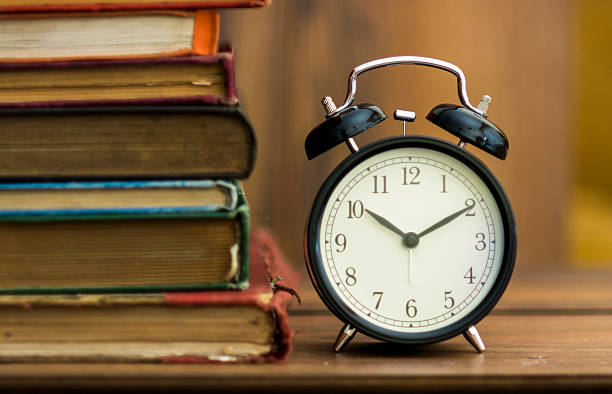 istock Black desk clock standing in front of the old book 510225751