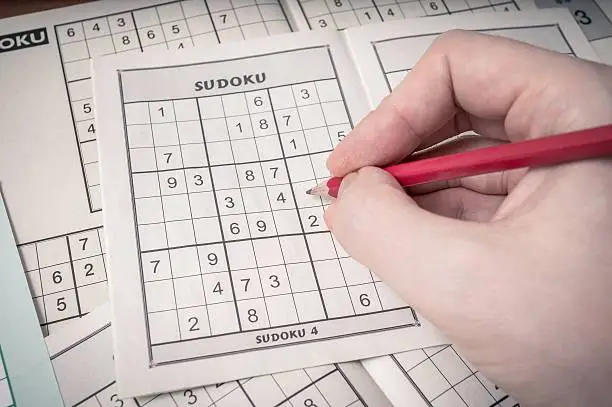 Photo of Hand holding pencil is solving sudoku crossword.