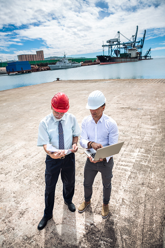 Two businessmen at commercial dock checking plans on computer.