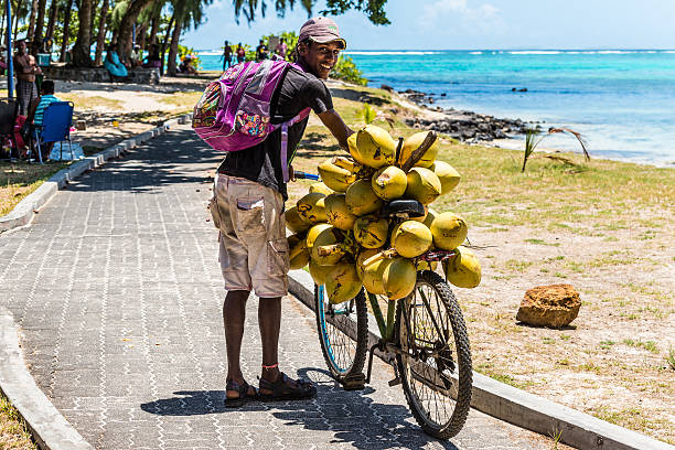 Blue Bay, Mauritius - December 27, 2015: Mauritius young man selling coconuts from his bike on the beach Blue Bay, Mauritius.
