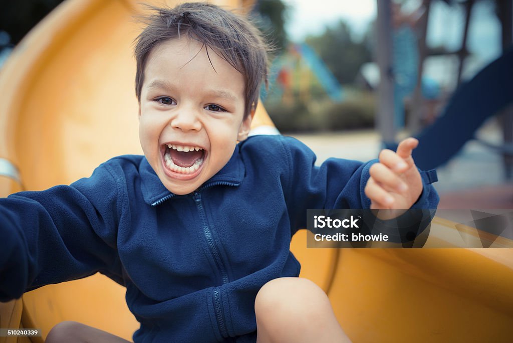 Cute 3 year old Asian boy plays on playground slide A young 3 year old Asian Caucasian boy plays on a yellow slide in a suburban playground on a cool cloudy day in Sydney, Australia Child Stock Photo