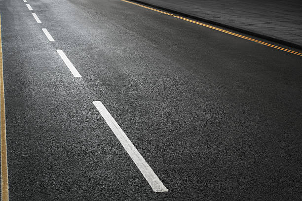 empty road Shot of an empty road with copy space for the designer with the texture of the tarmac and white and double yellow lines. lane marker stock pictures, royalty-free photos & images