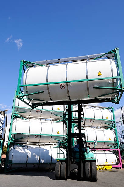 Forklift with driver loading blank container against clear sky.