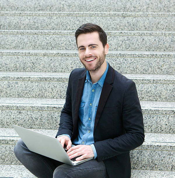 istock young man sitting on steps and smiling with laptop 510240857