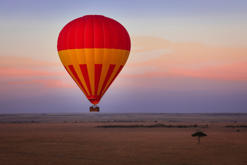 A hot-air balloon safari in progress at dawn on the Masai Mara in Kenya, East Africa; the sun has not as yet risen; but tourists are up in the sky looking for wild animals on the Mara. It is an ideal way to observe the animals as they are not disturbed by any noise.  Photo shot at the breaking of dawn from another hot-air balloon; horizontal format. Copy space.
