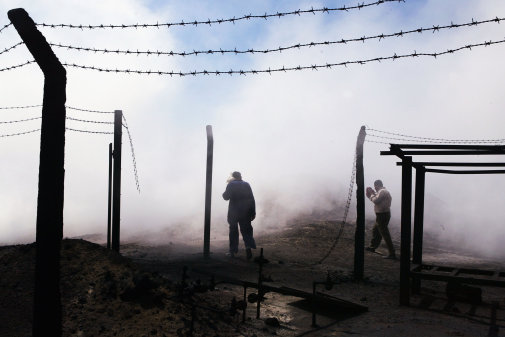 AL MUSAYYIB, IRAQ - JULY 05:  Iraqi firefighters walk past a burnt flow control station as smoke billows from an oil pipeline fire caused by insurgents who attacked the underground strategic oil pipeline, on July 05, 2004 near Al Musayyib, Iraq. Attacks on the oil industry, Iraq's main source of revenue, could hurt the new Iraqi interim government's attempt to boost the economy.  (Photo by Joe Raedle/Getty Images)