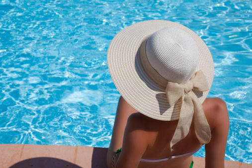 Woman in elegant big hat relaxing on the swimming pool. Enjoying summer sun and tanning