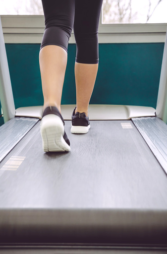 Back view of woman legs warming up over treadmill in a training session on fitness center
