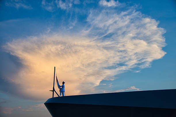 Singapore, Singapore - March 16, 2013: At the end of the day, a sailord goes through the lowering the country flag ceremony on board his modern navy vessel. The sailor is seen as a silhouette in front of a interestingly shapped cloud lit up by the last rays of the sun. The image was taken in Singapore. 