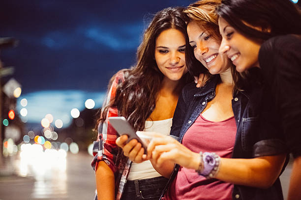 Teenage girls texting for Uber Teenage girls using taxi-hailing app at the street teenage girls dusk city urban scene stock pictures, royalty-free photos & images