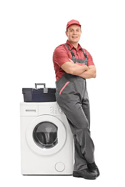 Full length portrait of a young male repairman leaning on a washing machine isolated on white background