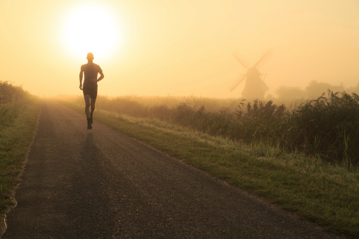 Man running in the foggy, Dutch countryside near a windmill.