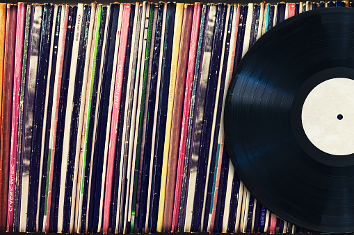 Caucasian female in nightwear holding a vintage vinyl record and drinking coffee at home in morning. Woman in pajamas looking at LP record and having morning coffee indoors.