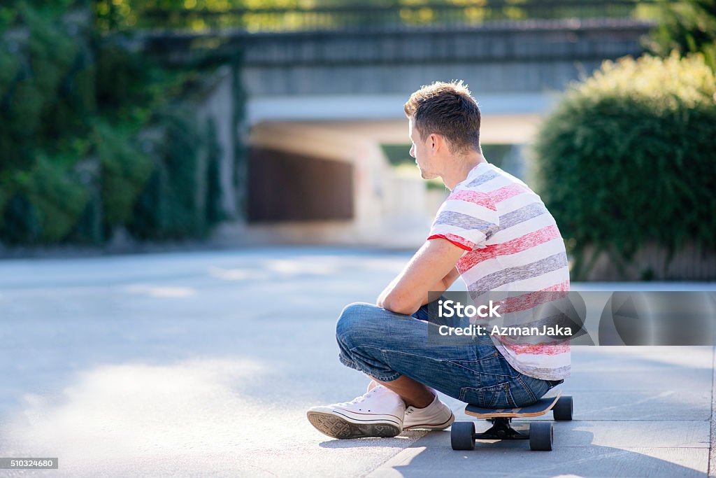 Skaterboy A side photo of a young man sitting on his skateboard and waiting 20-29 Years Stock Photo